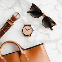 Stylish accessories arranged on a marble surface showcasing a handbag, sunglasses, watch, and belt photo