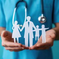 Family health concept represented by paper figures held by a doctor in a blue scrub with a stethoscope in hand photo