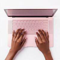 Person typing on a pink laptop with a clean workspace setup during daylight in a contemporary indoor environment photo