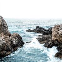 Secluded rocky coastline with gentle waves lapping at the shore during a cloudy day photo