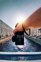 male hand holding a camera against the a river between old buildings to take a picture, pov, point of view perspective photo