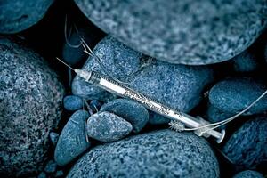 Discarded among the rocks in a park on a city street is a used syringe. photo