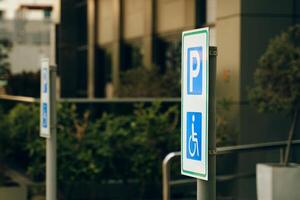 A street sign in electric blue font marks the reserved handicapped parking spot in front of the building on the grassy city road photo