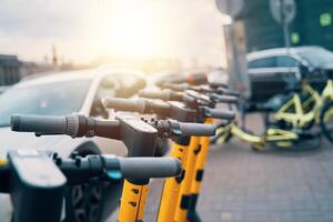 un fila de eléctrico scooters estacionado en el asfalto en frente de un auto, exhibiendo el mezcla de automotor Ingenieria y alternativa viaje máquina foto
