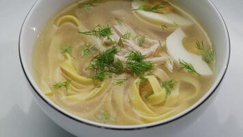 Fresh dill sprinkles over a steaming bowl of chicken soup filled with noodles and egg, creating a delicious meal video
