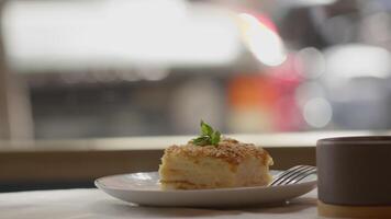 Napoleon cake rests on a cafe table by the window while customers walk by outside in an urban setting video