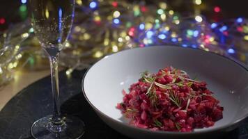 Beetroot salad with dill and a glass of sparkling wine stand on a table with a festive garland in the background video
