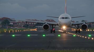 Airplane taxiing on the runway at dusk, illuminating the tarmac with its bright lights in the evening sky video