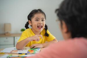 Joyful Child Engaged in Creative Drawing Activity with Adult in Bright Room, Showing Happiness and Artistic Expression through Colorful Artwork and Interaction photo