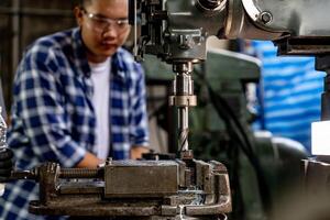 An Asian worker focuses on operating a drilling machine, ensuring quality output in a plant. photo