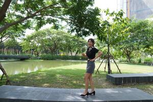 woman enjoying a moment of freedom, posing playfully on a green lawn in a sunny urban park, surrounded by trees and pathways, exuding a sense of joy and vitality. photo