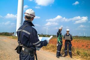 Two engineers in safety gear high-fiving against the backdrop of a towering wind turbine and clear blue sky, celebrating teamwork and renewable energy success in a sustainable environment. photo
