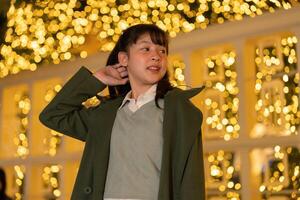 a young girl in a green coat standing in front of a christmas tree photo