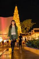 a young girl in a green coat and boots standing in front of a christmas tree photo