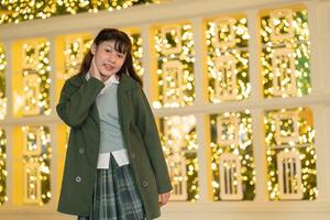 woman outdoors in a green coat, gesturing playfully against a backdrop of golden bokeh lights and a modern building, capturing a lively and festive urban atmosphere. photo