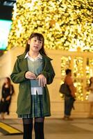 woman outdoors in a green coat, gesturing playfully against a backdrop of golden bokeh lights and a modern building, capturing a lively and festive urban atmosphere photo