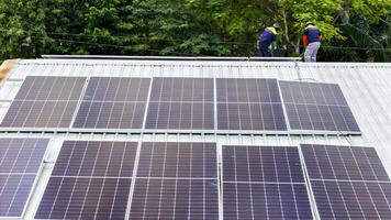 Solar panels installed on a corrugated metal roof, with technicians working amidst green trees, symbolizing the harmony between renewable energy and nature in a modern setting. photo