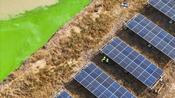 Aerial view of technicians worki ng under solar panels in a dry field, emphasizing renewable energy innovation, sustainable development, and environmental responsibility in a rural setting. photo