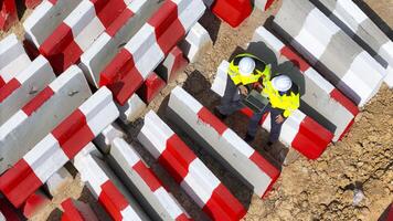 Close up top view of two construction workers in safety gear using a laptop at a worksite, surrou nded by red and white barricades, emphasizing teamwork, planning, and modern construction technology. photo