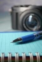 Close-up of a Pen on a Notebook with a Camera in the Background photo