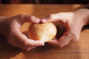 Two Hands Gently Cradling a Freshly Baked Bread Roll on a Rustic Wooden Table photo