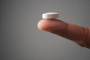 A detailed closeup image of a White Pill delicately Balanced on a Finger photo