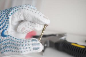 A hand gripping a screw while wearing safety gloves in a workshop setting photo