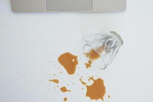 A drink was accidentally spilled on a desk with a laptop and glasses, creating a mess photo