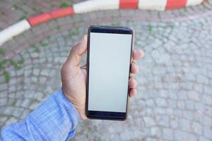 A person is holding a smartphone that has a blank screen while outdoors photo