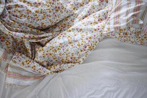A disheveled bed adorned with vibrant, colorful floral bedding and a striking green headboard photo