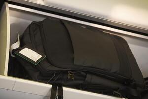 A black backpack has been conveniently stored in the overhead cabin space photo