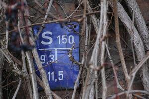 Historical gate valve sign for water supply in Germany, nearly overgrown by vines. The information on the sign give the type and position of a nearby underground gate valve. photo