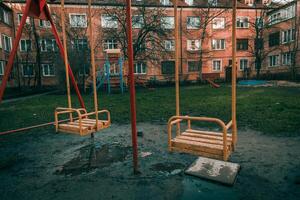 Children nice swing in empty courtyard of multi storey building, cloudy autumn day photo