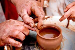 Potter sculpts mug from clay nice, close up dirty hands create vase on ceramist wheel photo