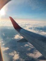 Experience the stunning panoramic view from a commercial airline wing on a serene morning flight, basking in sunlight above fluffy clouds, with a sprawling city skyline majestically below photo