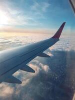 This stunning view showcases a morning flight with a planes wing above fluffy clouds, illuminated by vivid sunlight that brightens the sky and the city below, creating an enchanting atmosphere photo