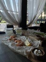 A delicious serving of shrimp garnished with lemon awaits on a rustic wooden table. Two refreshing drinks accompany the seafood, perfect for sharing at a meal photo