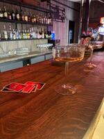 Two elegant cocktail glasses rest on a polished wooden bar, with UNO cards nearby. The vibrant backdrop suggests an inviting social setting perfect for games photo