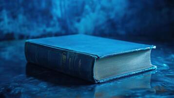 A blue book resting on a reflective surface against an abstract blue background at a quiet setting photo