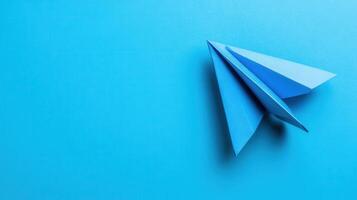 Bright blue paper airplane resting on a smooth blue surface under soft light photo