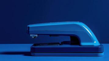 Stapler with a sleek design resting on a blue surface in a well-lit workspace setting during the day photo