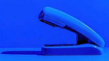 Bright blue stapler on a vivid blue background captured in a minimalistic style highlighting its design and color photo