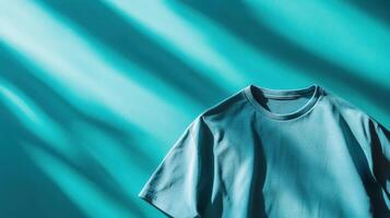 Soft teal t-shirt resting on a vibrant background with dynamic shadows created by light photo