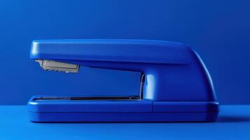 Blue stapler on a solid blue background showcasing a simple office supply essential photo