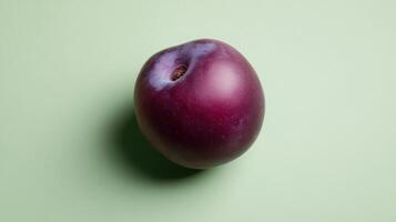 Fresh plum resting on a light green background showcasing its natural shine and color photo