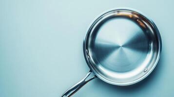 Stainless steel frying pan positioned on a light blue surface ready for cooking or preparation photo