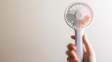 Hand holding a portable fan against a light background, providing relief from heat on a warm day indoors photo