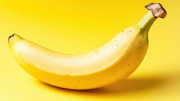 Yellow banana resting on bright yellow background, showcasing its curved shape and natural speckled texture photo