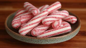 A colorful display of sugary peppermint sticks fills a bowl on a wooden surface photo