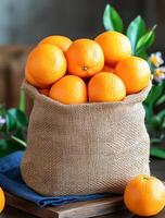 Oranges in a burlap sack. Freshly harvested oranges in a burlap sack displayed on a wooden table with green leaves and a blue cloth photo